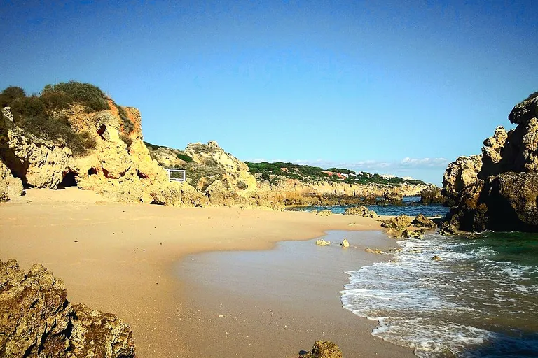 Falésias e ilhéus característicos da Praia dos Arrifes ao sol.