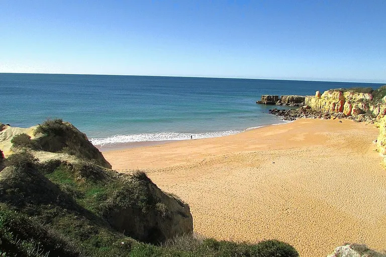 Cenário deslumbrante da Praia do Castelo, com falésias e mar azul do Algarve.